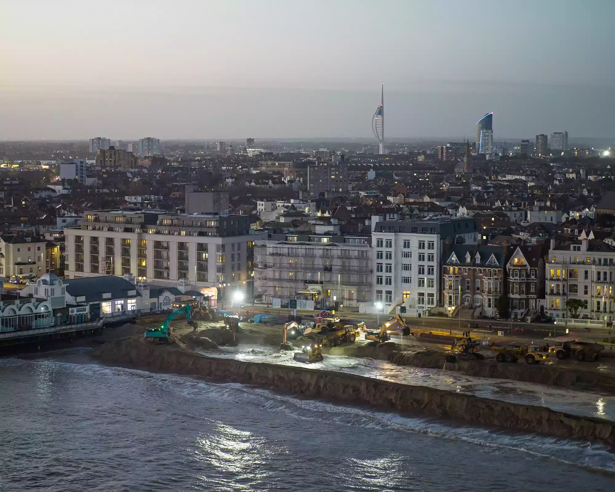 Aerial view of seafront construction works in Southsea at dusk, with excavators and earthmoving machinery beside the waterfront